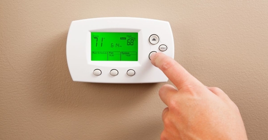 Woman turning down her thermostat to get cooler air in her home.